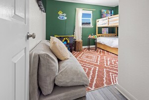 A room with a bunk bed, a sofa with cushions, a small table with a toy, and a window with a view.
