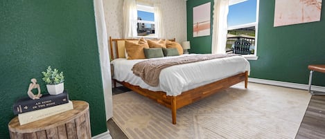 A bedroom with a wooden bed, green walls, a view through a window, and a small wooden stool with books.