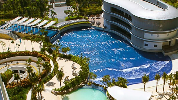 Un complexe hôtelier doté d’une grande piscine, d’un espace dédié aux toboggans aquatiques et d’une plage avec des chaises longues.