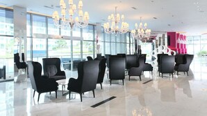 Un hall d’entrée moderne, doté de fauteuils en cuir noir, de grands lustres et d’un intérieur lumineux et spacieux, avec de grandes fenêtres.