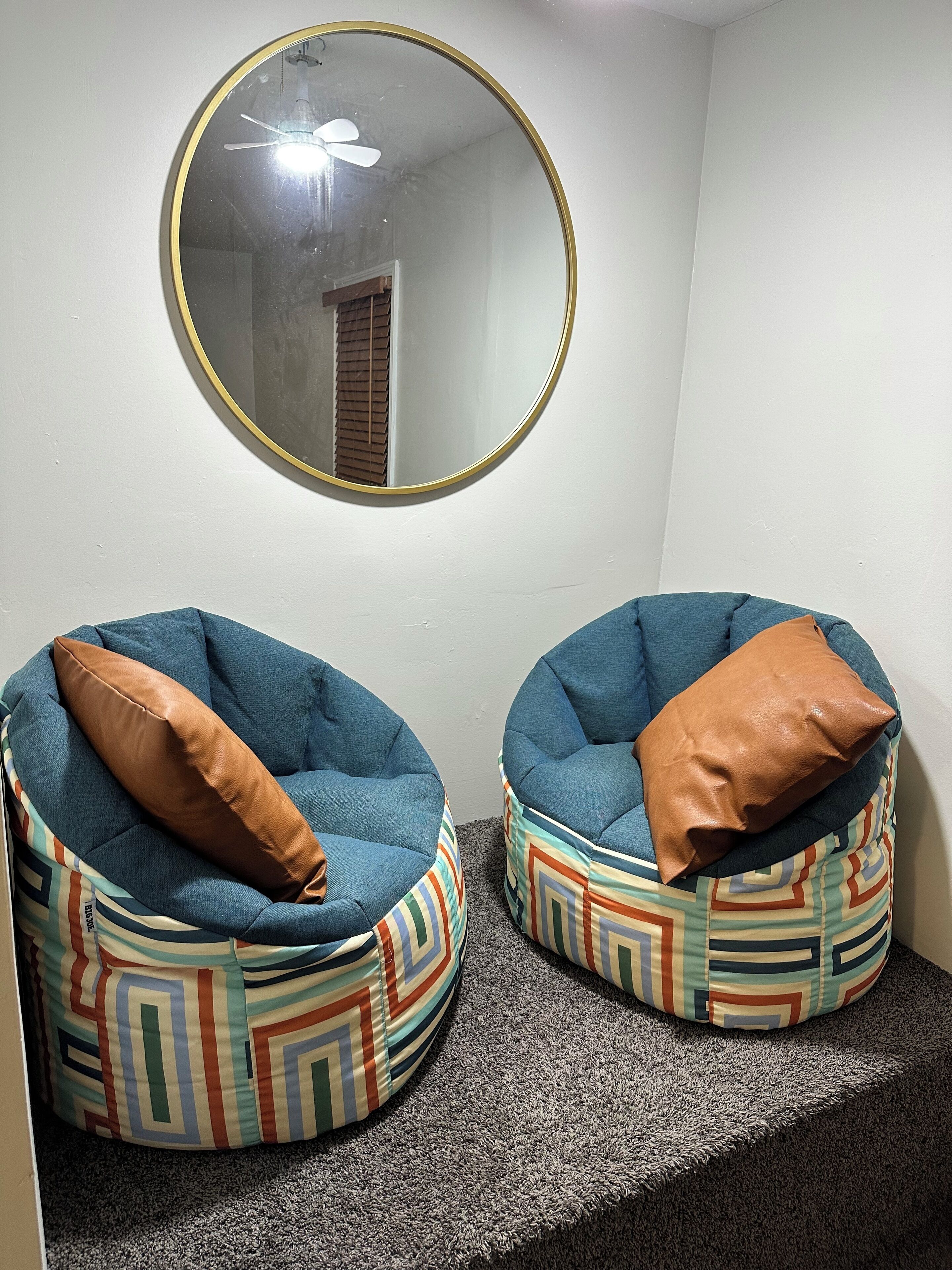 Two bean bag chairs with patterned cushions, a round mirror with a gold frame, and a ceiling fan.