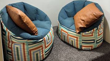 Two bean bag chairs with patterned cushions, a round mirror with a gold frame, and a ceiling fan.