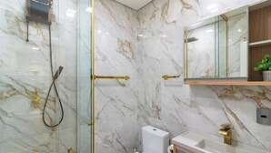 A modern bathroom with marble walls, a glass shower enclosure, a toilet, and a sink with a gold faucet. - Apt With Barbecue 200 m From the Beach Ifa0054 (Penha)