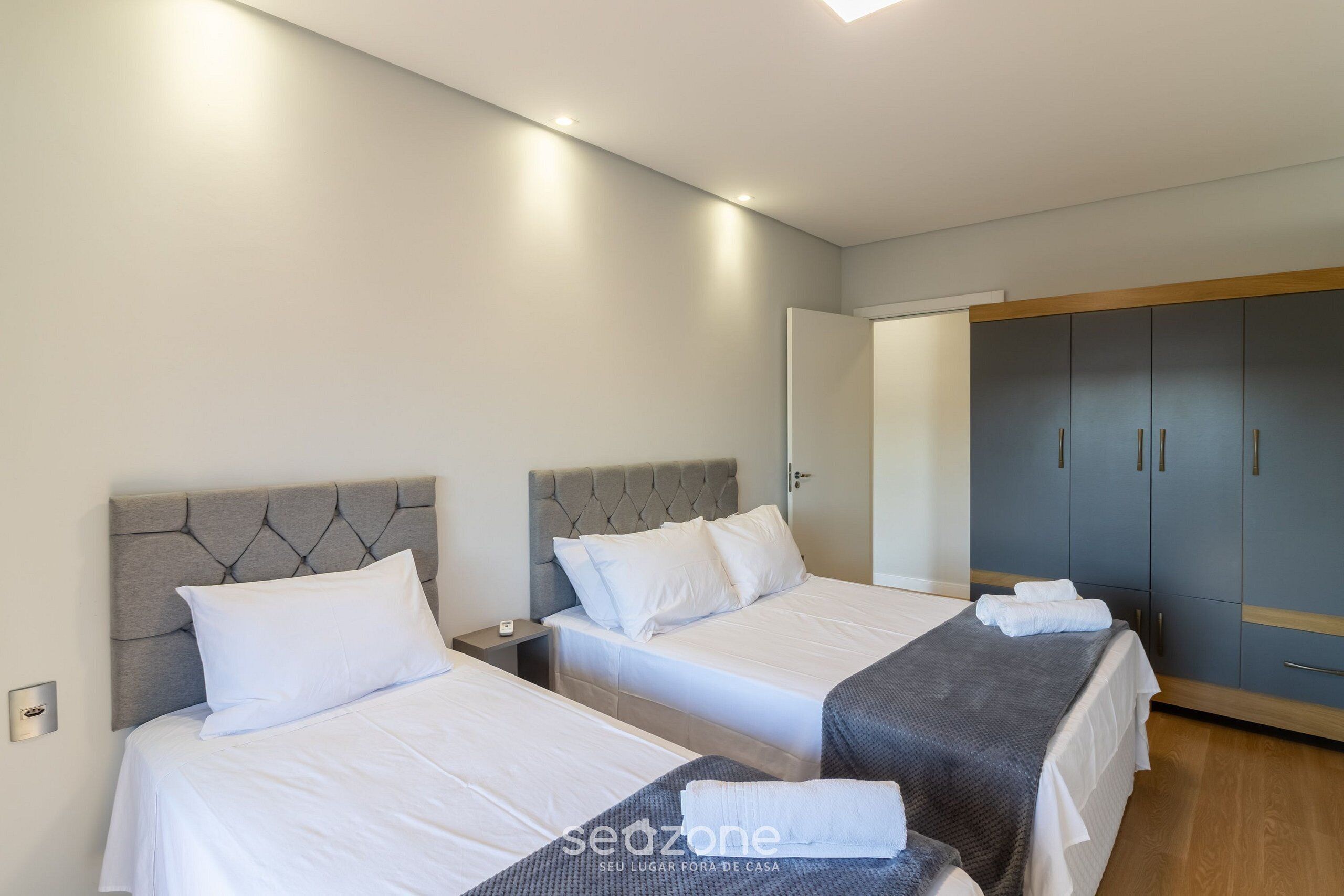 A hotel room with two beds, a wardrobe, and a bedside table.