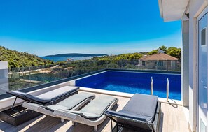 Une piscine sur le toit, dotée de chaises longues, offrant une vue dégagée sur la mer et un paysage montagneux.