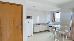 A modern kitchen with white cabinets, a microwave, and a sink. There is a wooden door on the left and a window on the right. - Caldas Novas - Golden Dolphin Supreme (Caldas Novas)