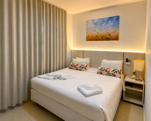A hotel room with a large bed, a painting of wheat on the wall, a bedside table with a lamp, and a nightstand with a phone. - Caldas Novas - Golden Dolphin Supreme (Caldas Novas)
