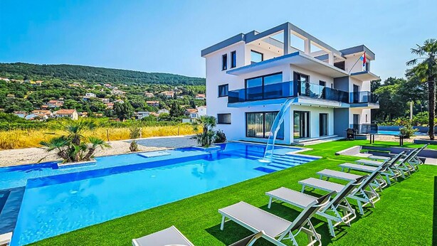 Ein modernes, zweistöckiges Haus mit Swimmingpool und Liegestühlen.