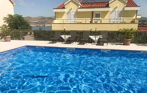 A swimming pool with lounge chairs and a view of a building with a red-tiled roof. - Stunning apartment in Okrug Gornji with outdoor swimming pool (Okrug Gornji)