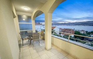 A balcony with a table and chairs, overlooking a body of water and distant hills. - Stunning apartment in Okrug Gornji with outdoor swimming pool (Okrug Gornji)