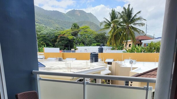 Ein Balkon mit zwei Korbstühlen und Blick auf ein Wohngebiet mit Gebäuden und einem Berg im Hintergrund.