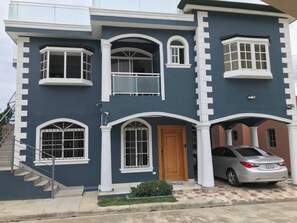 A two-story house with a staircase leading to the entrance, a car parked in the driveway, and a small garden area. - Tranquil 1-bedroom Apartment in Puerto Plata, Dominican Republic (Puerto Plata)