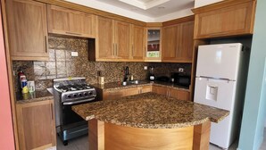 Eine moderne Küche mit Holdekor-Schränken, Granit-Arbeitsplatten, einem Edelstahlherd, einem Samsung-Kühlschrank und zwei roten Barhocker.