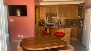 Eine moderne Küche mit Holzschränken, einer Granit-Arbeitsplatte und einem eingebauten Backofen. Ein Esstisch mit zwei Stühlen steht daneben.