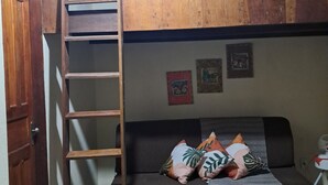 Et værelse med en køjeseng, en træstige, en sofa med hynder og et lille bord med en lampe.