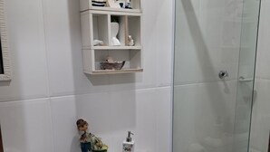 Et badeværelse med toilet, en hylde med dekorative genstande, en bruseforhæng af glas og et lille rundt bord med hæklet dækken.