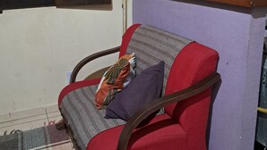 En hyggelig opholdsstue med en rød lænestol, et ternet tæppe, et vindue med skodder, en kaffemaskine og en reol med krus.