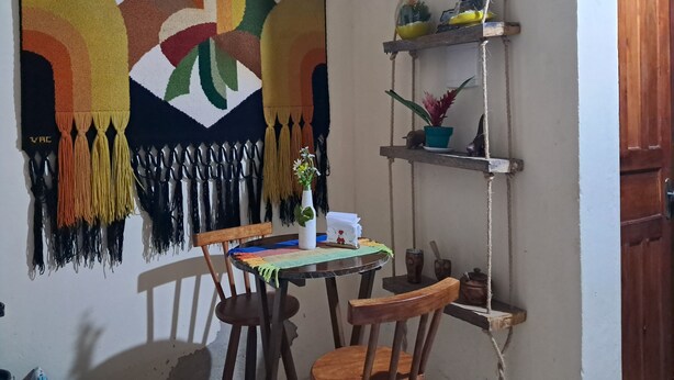 Et spiseområde med et bord, stole, et farverigt gobelin og reoler med planter.