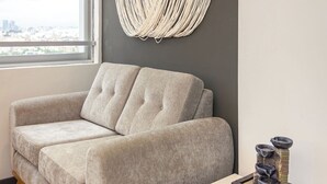 Una sala de estar moderna con un sofá gris, una mesa de centro de madera con una revista, y un colgador de macramé en la pared.