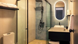 Un baño moderno con ducha de vidrio, inodoro y lavamanos con espejo.