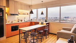 Una cocina moderna con una isla grande, taburetes de bar y vistas a la ciudad a través de amplios ventanales.