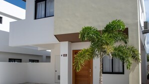 Edifici modern de dos pisos amb teulada plana, un petit arbre al jardí davanter i un vial pavimentat.