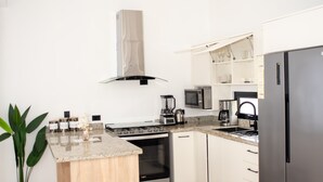 Una cuina moderna amb armaris blancs, un frigorífic d'acer inoxidable, un forn encastrat, microones i una cafetera.