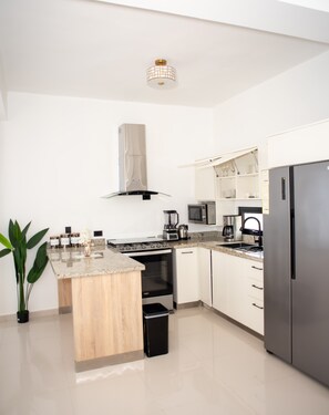 Una cocina moderna con armarios blancos, un refrigerador de acero inoxidable, horno empotrado, microondas y cafetera.
