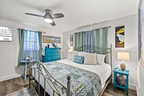 Ein Schlafzimmer mit Bett, Kommode, Nachttisch, Deckenventilator und Kunstwerken an den Wänden.