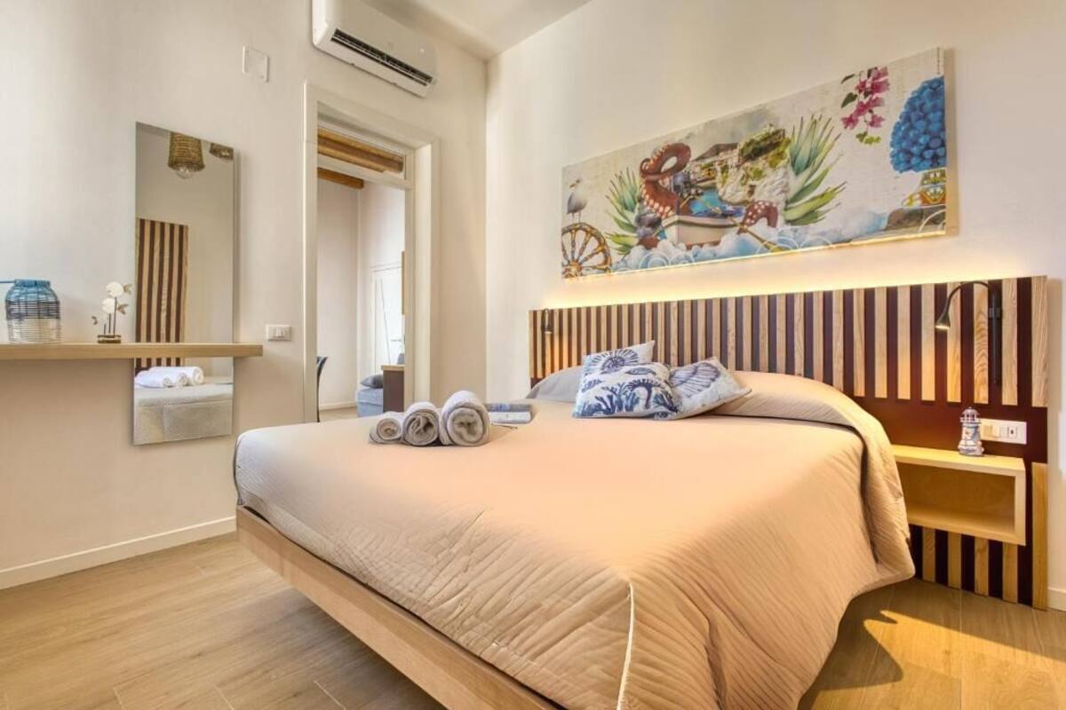 A bedroom with a large bed, a wooden headboard, a painting above the bed, and a mirror on the wall.