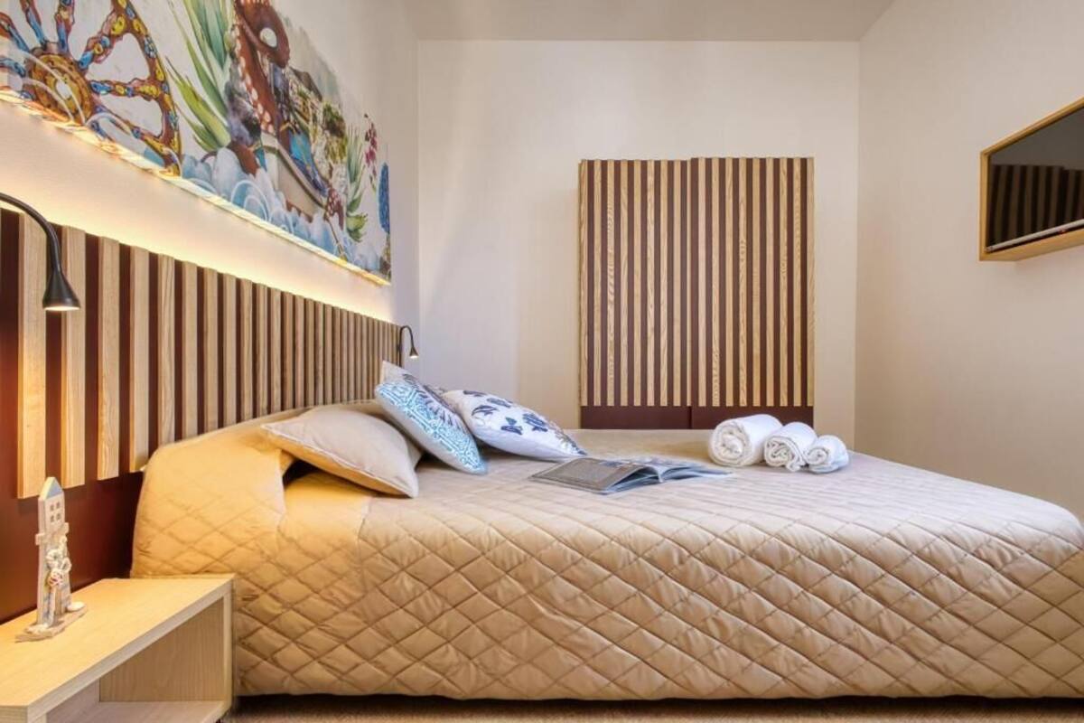 A hotel room with a large bed, a nightstand, a wall-mounted lamp, a painting, and a striped panel.