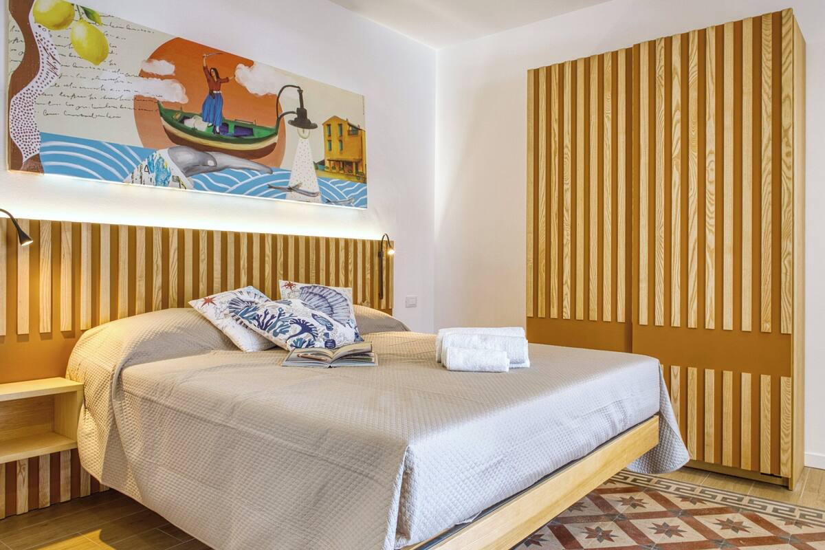 A hotel room with a bed, a wooden headboard, a patterned floor, and a wall with a painting.