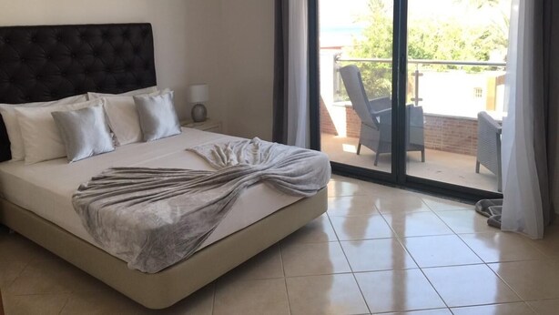 A hotel room with a large bed, a nightstand, and a view of the outdoor balcony. - Lali's House (Tarrafal)