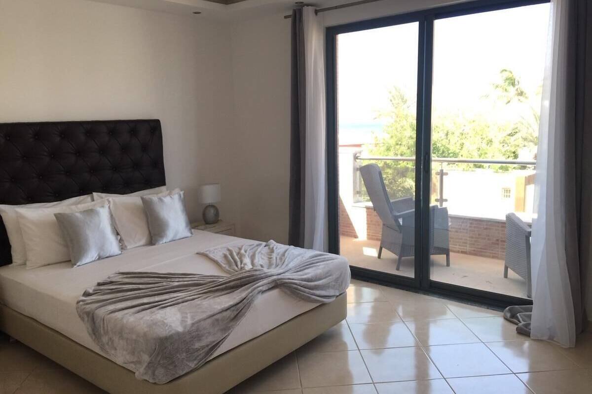 A hotel room with a large bed, a nightstand, and a view of the outdoor balcony.