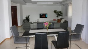 A modern living room with a dining area, a flat-screen TV mounted on the wall, and a potted plant. - Lali's House (Tarrafal)