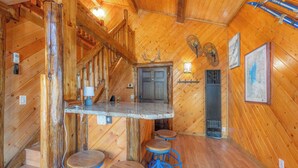 Interno di una baita in legno con una scala, sgabelli da bar in legno, angolo cottura e porta sci a parete.