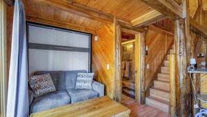 Un accogliente interno di una baita con una scala in legno, un divano con cuscini decorati e un settimino in legno.