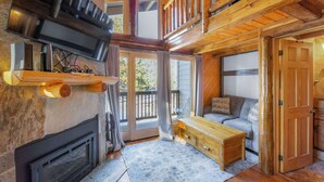L'interno accogliente di una baita con camino, arredi in legno e un balcone con vista su un paesaggio suggestivo.