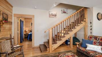 A cozy living room with a wooden staircase, a patterned sofa, and a rocking chair.
