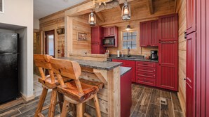 Eine rustikale Küche mit Holzwänden, einem schwarzen Kühlschrank, roten Schränken und einem hölzernen Barhocker.