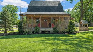 A log cabin with a porch, surrounded by a well-maintained lawn and trees.