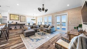 A spacious living room with a large sofa, a coffee table, and a view of the sea through large windows. - Waterfront Views - Walk to Beach - Heated Pool (Gulf Shores)