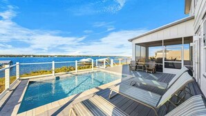 A modern outdoor pool area with a view of the sea, lounge chairs, and a covered seating area. - Waterfront Views - Walk to Beach - Heated Pool (Gulf Shores)