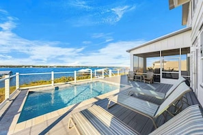 Ein moderner Poolbereich im Freien mit Meerblick, Liegestühlen und einer überdachten Lounge.