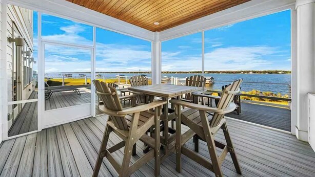 A covered outdoor dining area with a wooden table and chairs, large windows, and a view of the water. - Waterfront Views - Walk to Beach - Heated Pool (Gulf Shores)