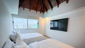 Une chambre avec deux lits, une grande fenêtre et un téléviseur à écran plat fixé au mur.