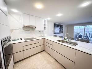 A modern kitchen with white cabinetry, a marble backsplash, and a built-in oven. - Luxe Punta Hansa PH (San Andrés)