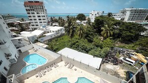 Un espace piscine sur le toit, comprenant plusieurs piscines, entouré d’immeubles et de palmiers, et offrant une vue imprenable sur la côte.