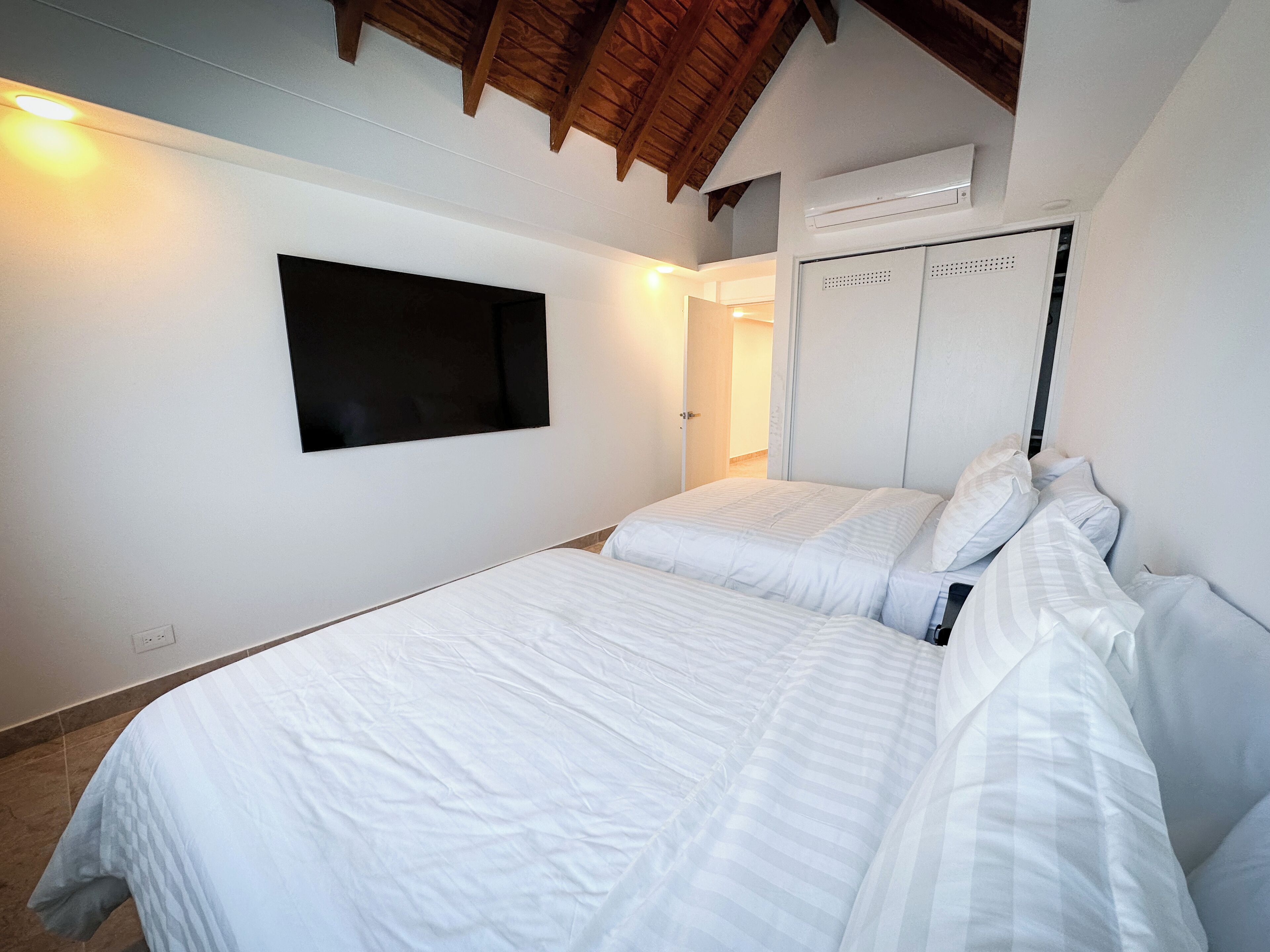 A bedroom with two beds, a mounted TV, and a wardrobe with a mirror.