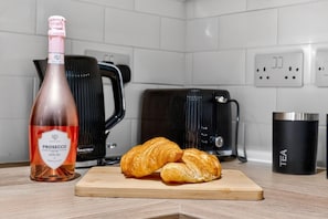 A kitchen counter with a bottle of Prosecco, two croissants, a black coffee maker, and a black thermos labeled "TEA". - Luxury 2BR Flat - Fast Wi-Fi - Work Area (Cardiff)